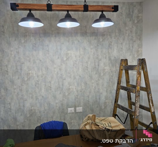 קיר עם טפט אפור, סולם ועבודות נייר על שולחן